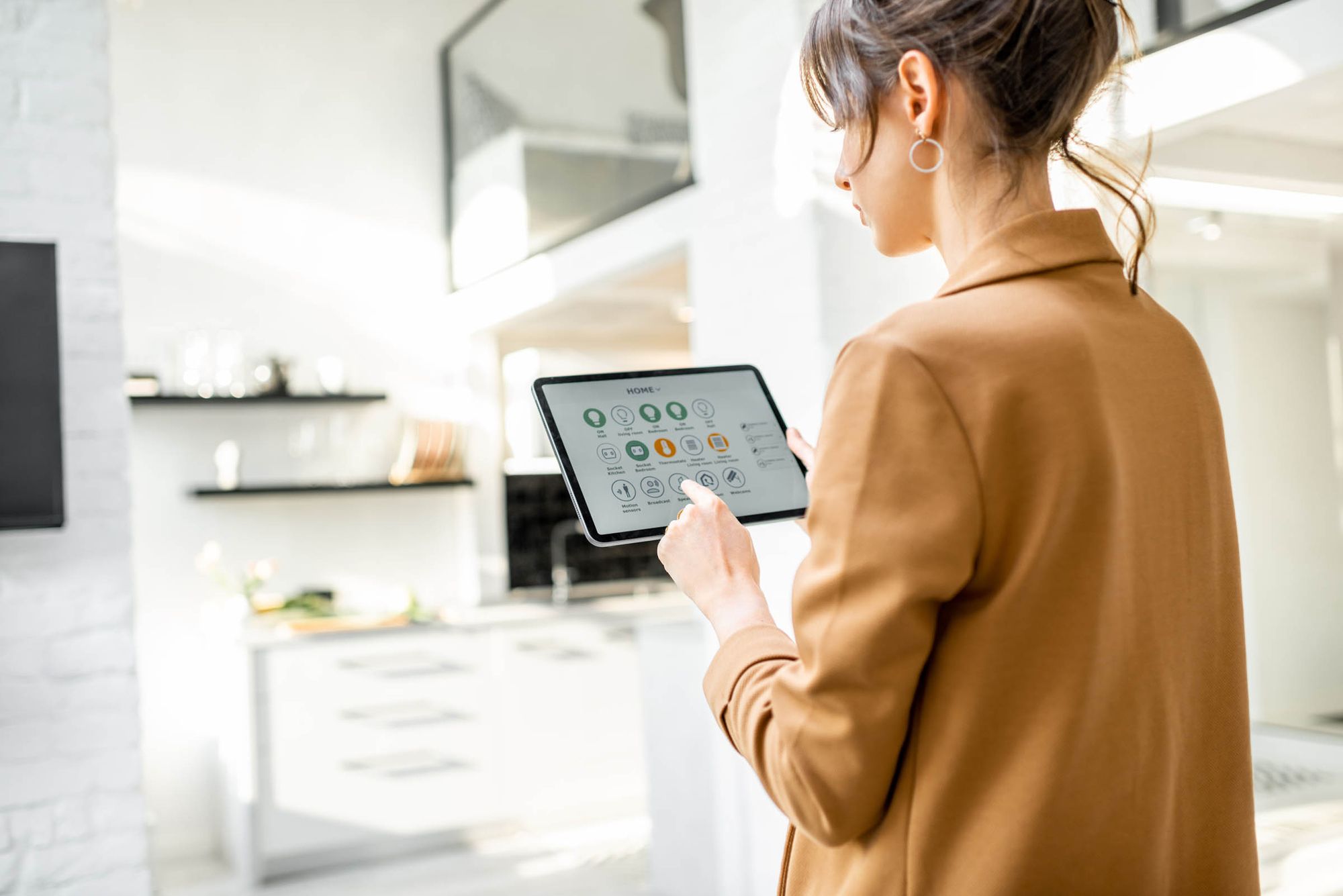 Eine Person mit braunem Blazer hält ein Tablet mit einer Benutzeroberfläche, die verschiedene Symbole für Energie und Elektrogeräte zeigt.